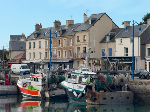 Deux bateaux de pêches sont amarrés sur le bassin de Port-en-Bessin, avec en fond des bâtiments et des commerces.