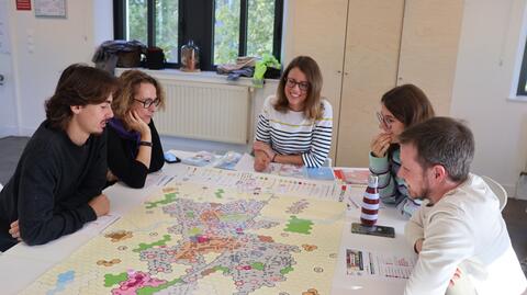 Les étudiantes et étudiants de quatrième année IN SITU, mélangés avec des professionnels de l'aménagement territorial venus de différentes régions, sont assis autour d'une table sur laquelle est posée une grande carte et des jetons. 